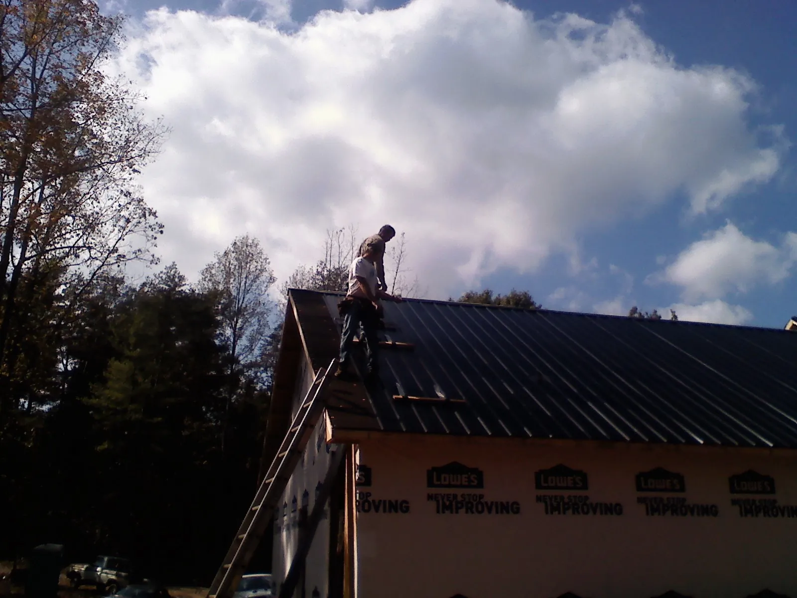Roofer fastening dark metal panels high against a cloudy sky, from a Roof Inspection job in Marion