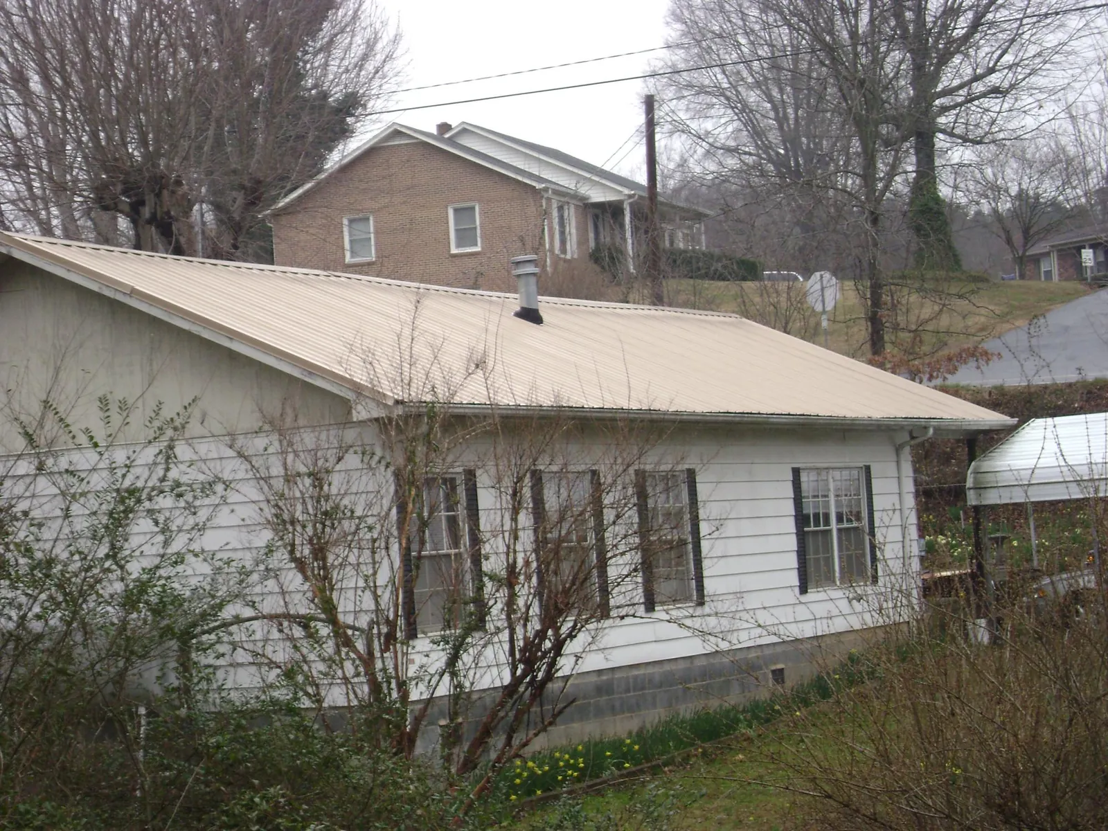 Tan metal roof on a white sided house set into a hillside — Commercial Roofing by Roofing Brothers in Marion